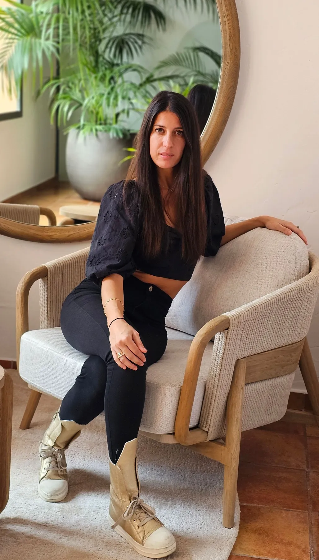 Laura sentada en un sillón junto a un espejo redondo y plantas